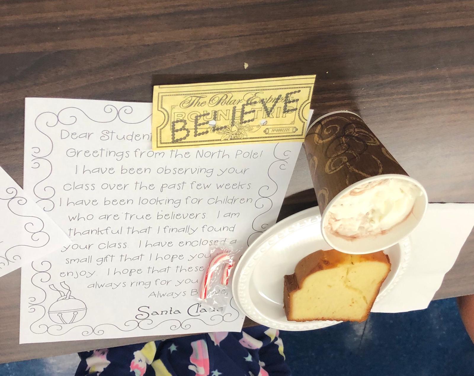close up of letter from santa, believe ticket, bell on red string, pound cake and hot cocoa with whipped cream