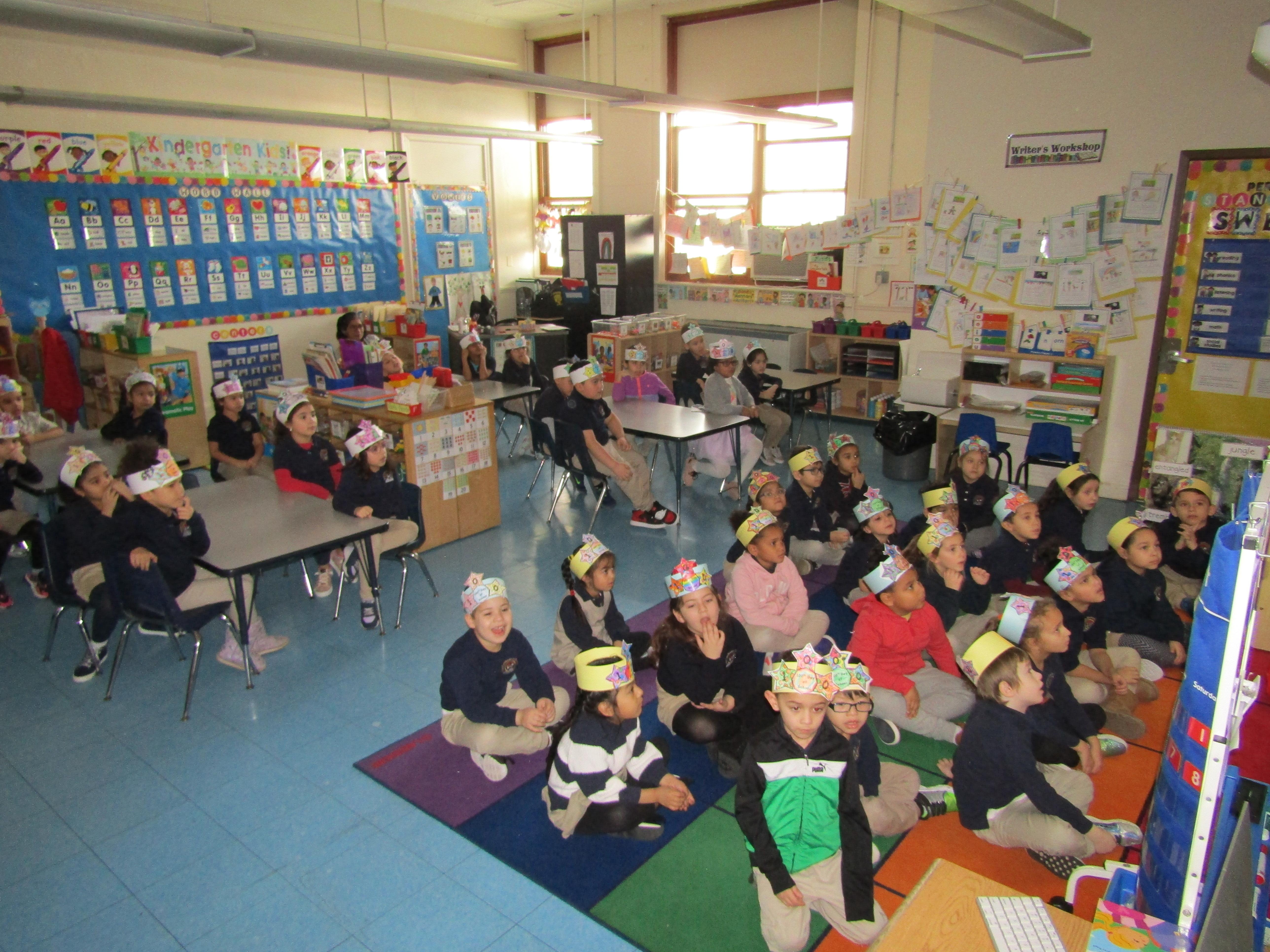 Kindergarten classes listening to teacher read a story while wearing hats 100