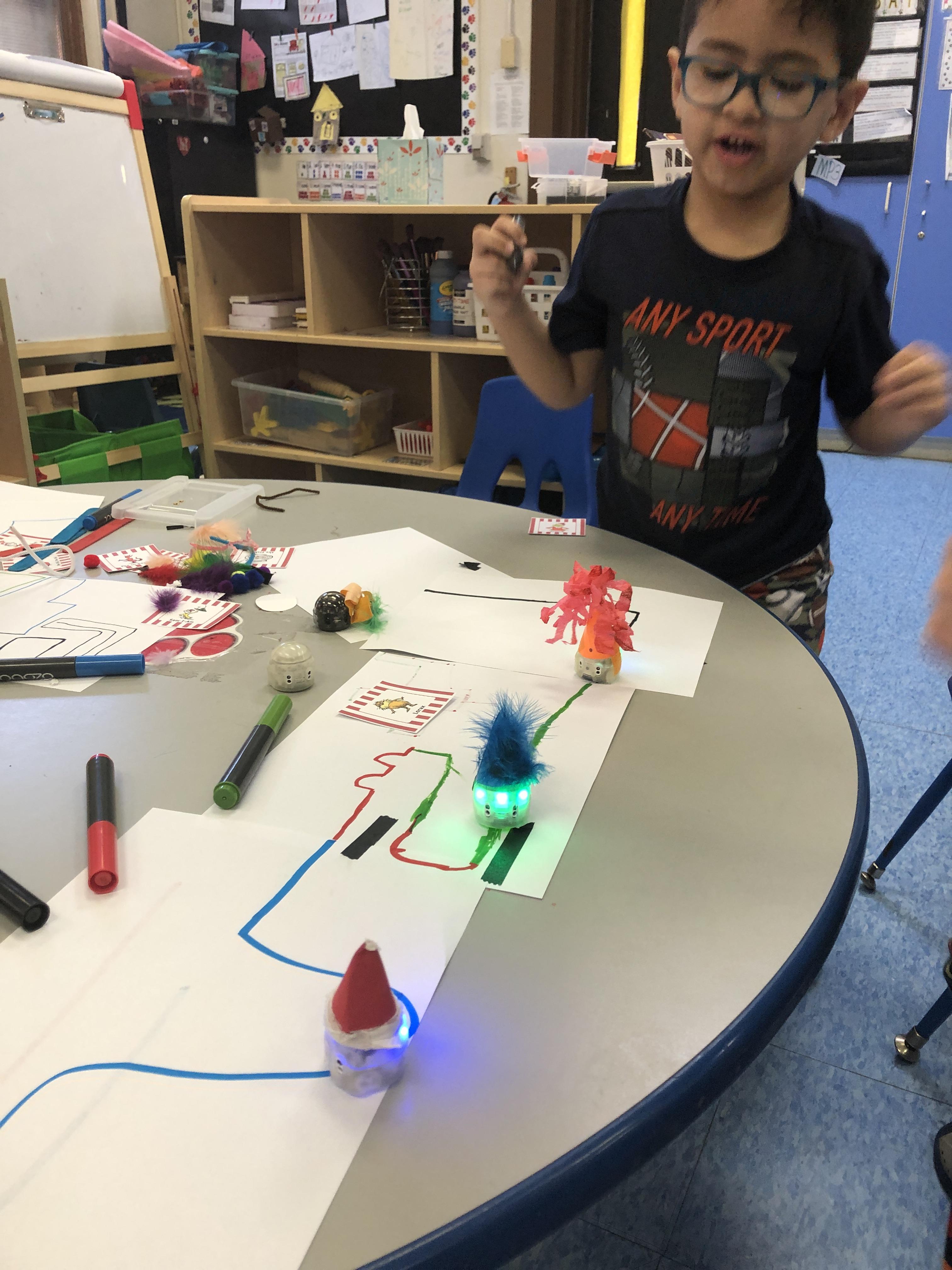 boy with glasses looking at the two ozobots on the trail he designed