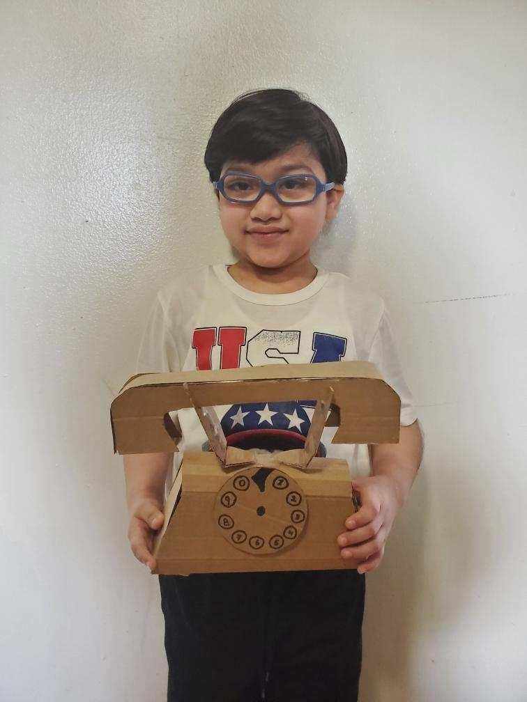 boy with glasses holding up a cardboard old rotary phone
